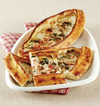 Beyaz bir tabakta bir Türk pidesi servis edilir. Ekmek tekne şeklindedir, üstüne otlar ve baharatlar eklenir ve birkaç dilim kesilerek yan yana dizilir. Tabağın altında kırmızı ve beyaz bir bez kısmen görünür.